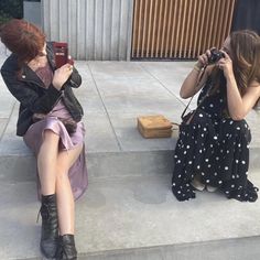 two women sitting on steps taking pictures with their cell phones