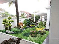 a garden with grass, rocks and trees in front of a white fenced area