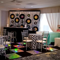 a room filled with lots of white chairs and tables covered in colorful cloths on top of checkered flooring