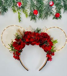 a mickey mouse ears headband with red flowers and greenery on the side, surrounded by christmas decorations