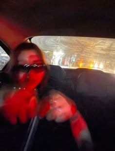 a woman driving in the back seat of a car with red face coverings on