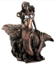 a statue of a mermaid holding a fish in her hand and sitting on a rock