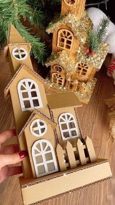 someone is holding up a cardboard model of a house in front of a christmas tree