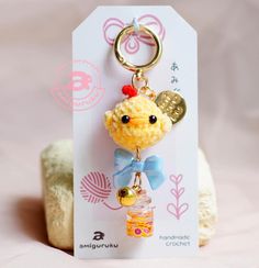 a keychain with a small yellow chicken on it's head and a blue bow around its neck