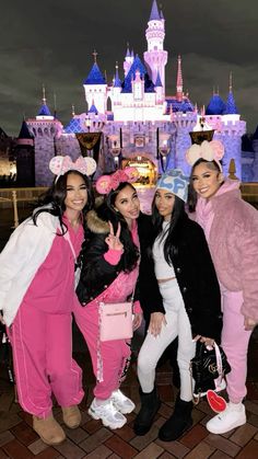 four women in pink and white outfits posing for a photo at disney world with the castle in the background