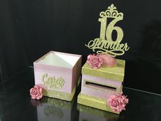 two pink and gold boxes with flowers on them sitting on a black table next to each other