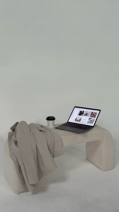 an open laptop computer sitting on top of a white bench next to a pillow and blanket