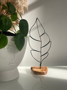 a plant in a white vase next to a wire sculpture with a wooden stand on it