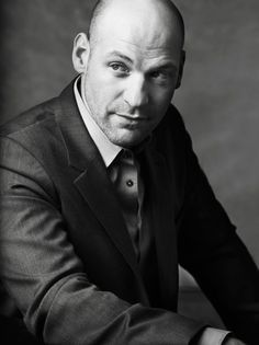 a bald man in a suit and tie posing for a black and white photo with his hands on his knees