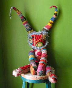 a multicolored stuffed animal sitting on top of a wooden stool next to a green wall