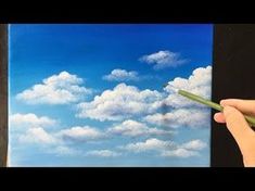 a person is holding a pencil in front of a painting with clouds and blue sky