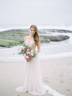 a woman standing on top of a beach next to the ocean holding a bouquet of flowers