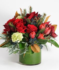 a green vase filled with red roses and greenery