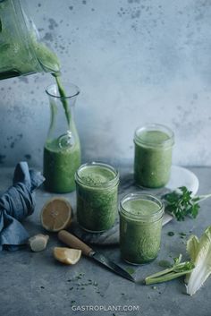 three jars filled with green smoothie on top of a table next to other ingredients