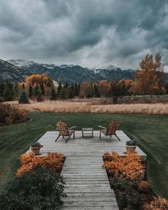 two wooden chairs sitting on top of a wooden walkway next to a lush green field