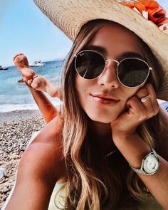 a woman wearing sunglasses and a straw hat on the beach with her hand under her chin