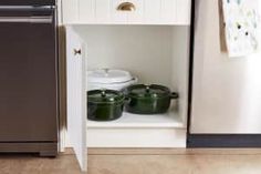 pots and pans are sitting in the corner of a kitchen cabinet next to an open refrigerator