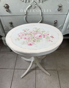 a white table with pink flowers painted on it and an old dresser in the background