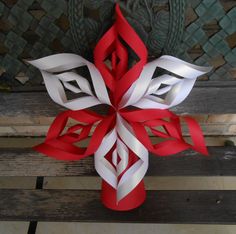 a red and white paper snowflake sitting on top of a wooden bench next to a wall