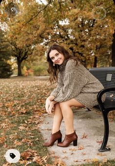 a woman is sitting on a bench in the park with her legs crossed and wearing brown boots