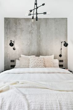 a bed with white sheets and pillows in a room that has concrete walls on both sides