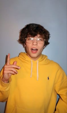 a young man in a yellow hoodie is making the peace sign with his fingers