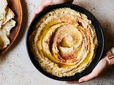 two hands holding a bowl of hummus and tortilla chips