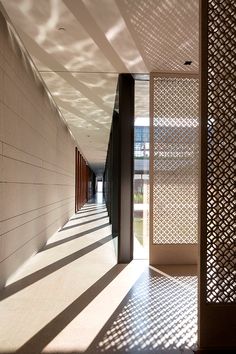 an empty hallway with white walls and shadows on the wall, leading to another room