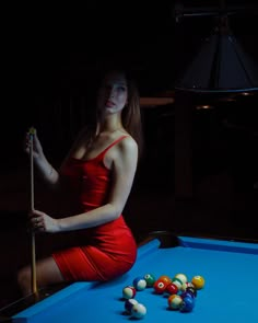 a woman in a red dress sitting on top of a pool table holding a cue