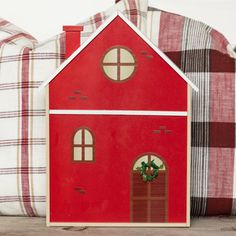 a red doll house sitting on top of a wooden table next to two plaid pillows