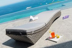 an outdoor chaise lounge with drinks on the table next to it, overlooking the ocean