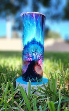 a glass sitting in the grass with a tree painted on it's bottom half