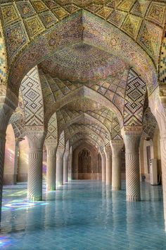 the inside of an ornate building with columns and tiled walls, surrounded by blue water