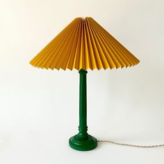 a green table lamp with a yellow shade on the base and a white wall behind it