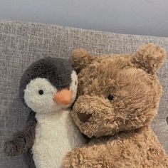 two stuffed animals sitting next to each other on a couch with one penguin hugging the other