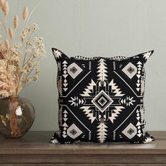 a black and white pillow sitting on top of a wooden table next to a vase