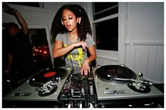 a woman in grey shirt standing next to a dj's turntable