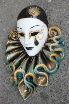 a white mask with black and gold designs on it's face sitting on the ground