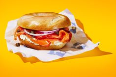 a sandwich with meat, cheese and tomatoes on a yellow paper wrapper against a bright background