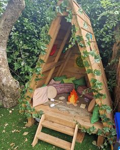 a small wooden structure with plants growing on the roof and in front of it is a fire pit surrounded by greenery