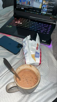 a laptop computer sitting on top of a bed next to a cup of coffee and a bag of chips