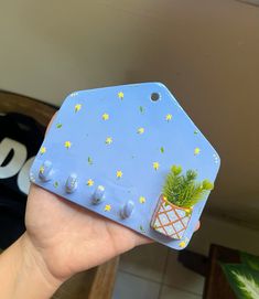 a hand holding up a small blue object with yellow stars and a potted plant on it