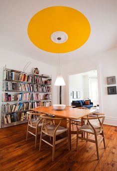 a dining room table with chairs and bookshelves in the background, under a yellow ceiling light