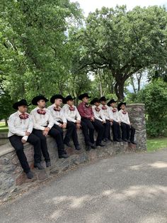 a group of men in cowboy hats sitting on a stone wall with trees in the background