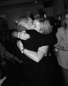 black and white photograph of two women hugging each other in front of a group of people