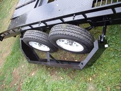 two large tires are attached to the back of a utility trailer that is parked on grass