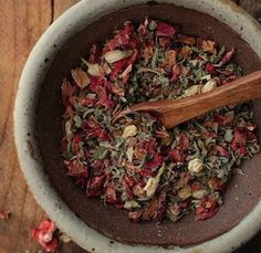 a wooden spoon is in a bowl filled with various types of flowers and herbs on a table