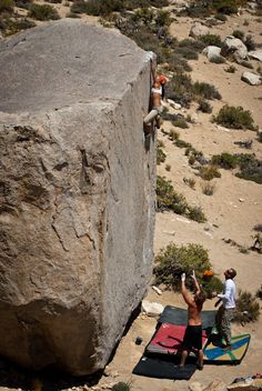 two people climbing up the side of a large rock