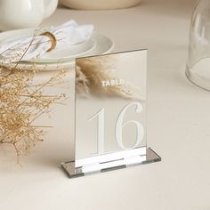 a glass table number sitting on top of a table next to a vase with dried flowers