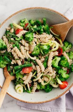 a pasta salad with broccoli and tomatoes in a white bowl on a marble table